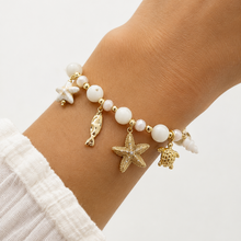 Bracelet Aphros - perles blanches rondes et facettées intercalaires dorées 5 charms marins porté au poignet - LELIEGE